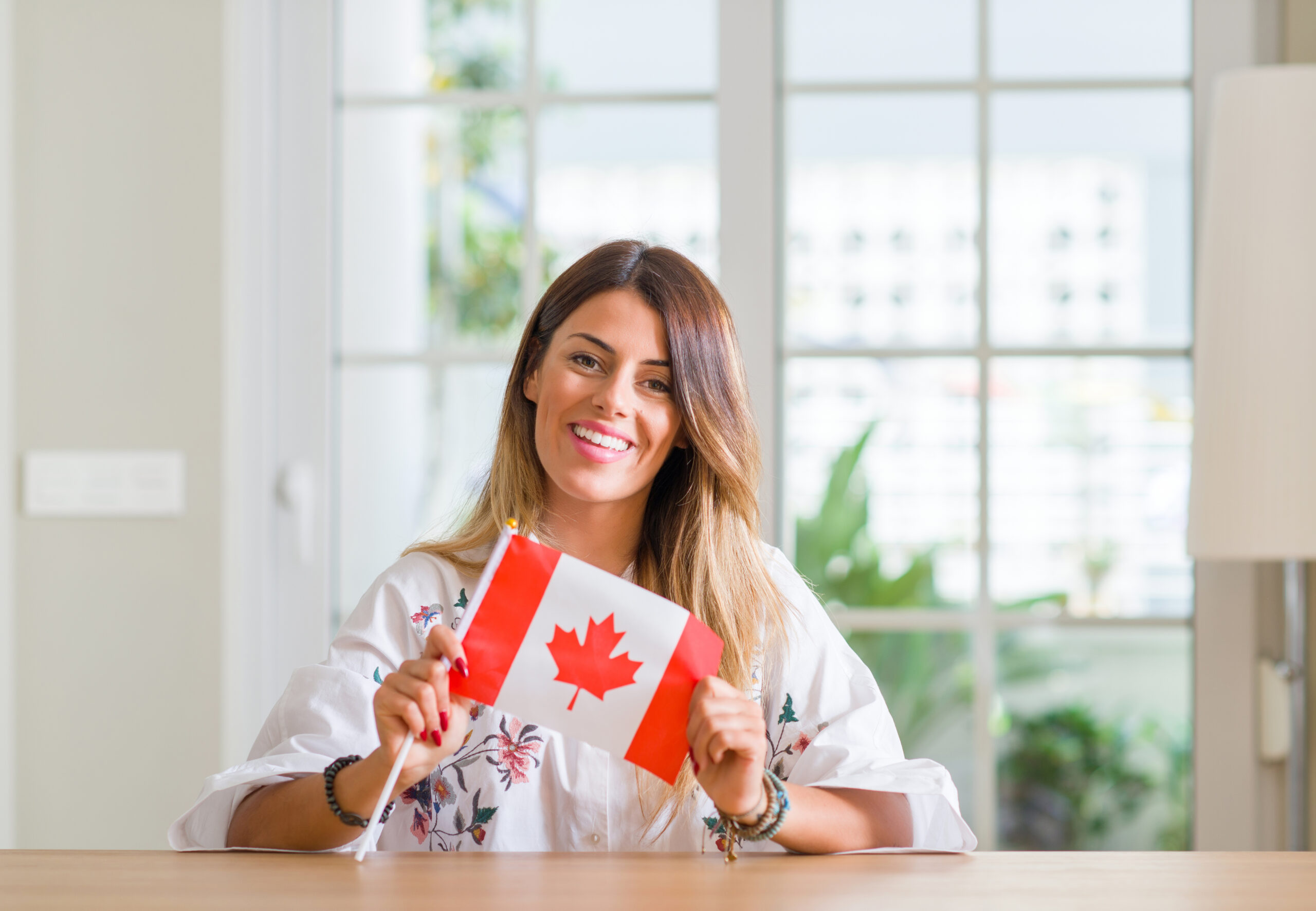 Smiling woman holding a small Canadian flag, representing Canadian identity and dental care options in the context of the Canadian Dental Care Plan (CDCP).