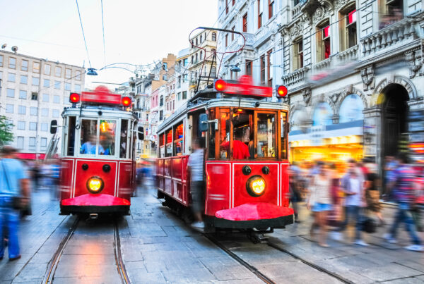 Red trams navigating a busy street in Istanbul, with blurred pedestrians and historic buildings, symbolizing vibrant urban life and accessibility in dental tourism.