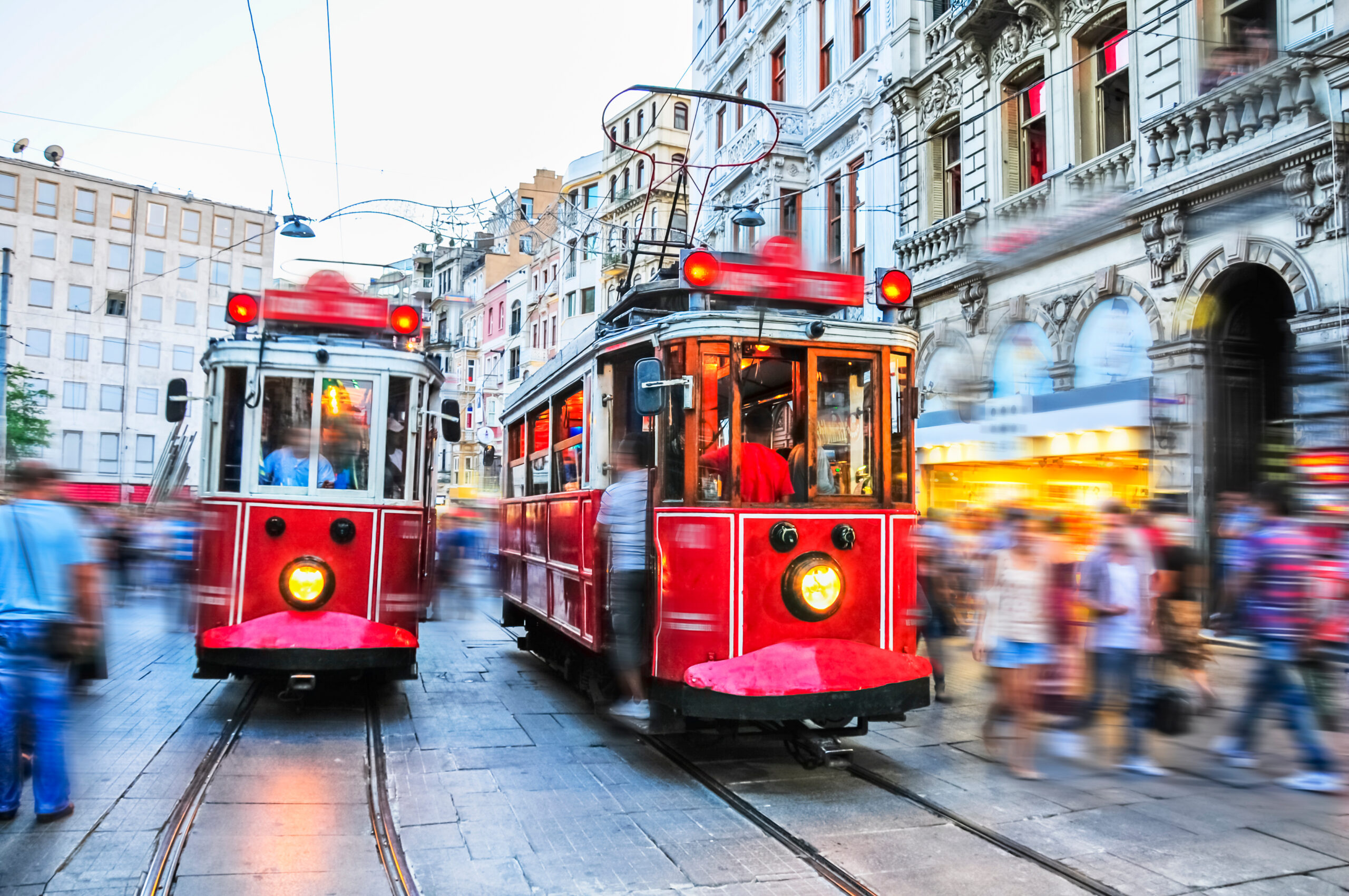 Red trams navigating a busy street in Istanbul, with blurred pedestrians and historic buildings, symbolizing vibrant urban life and accessibility in dental tourism.