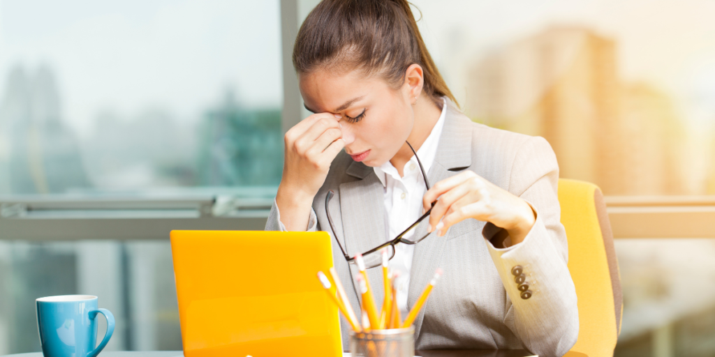 Woman experiencing jaw tension and headache at work, a common symptom of bruxism and teeth grinding.