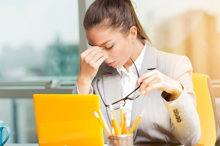 Woman experiencing jaw tension and headache at work, a common symptom of bruxism and teeth grinding.