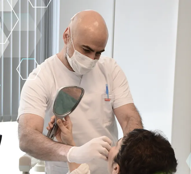 Dentist, Dr. Can Atakan of a clinic in Istanbul, treating a patient holding a mirror to their face.