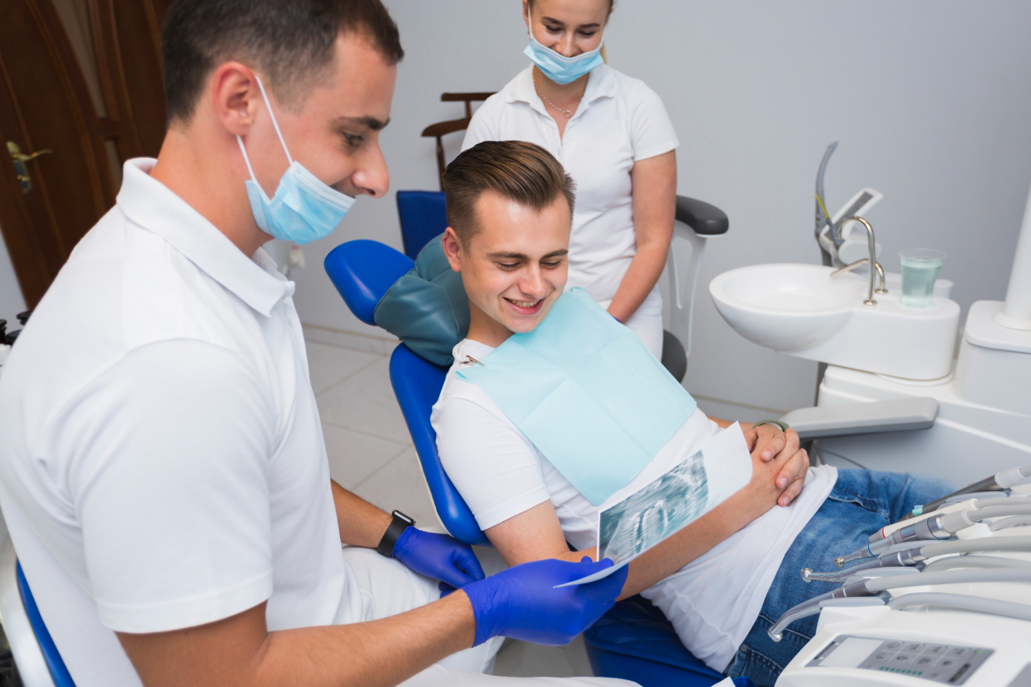 Dental patient smiling while viewing X-ray with dentist and assistant in modern clinic, emphasizing quality dental care experience in Turkey.